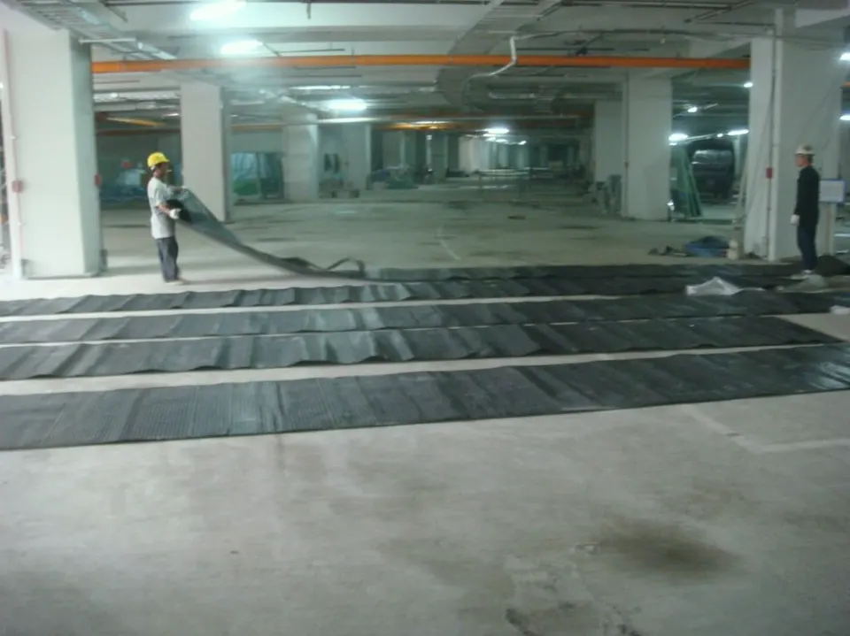 地下停車空間地面上攤開成列的黑色板材，一位人員拉起其中一條