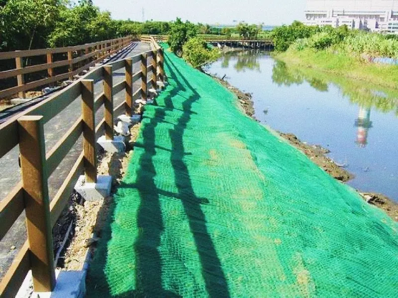 綠色抗沖蝕網鋪設於河岸邊坡，旁邊為步道木欄杆