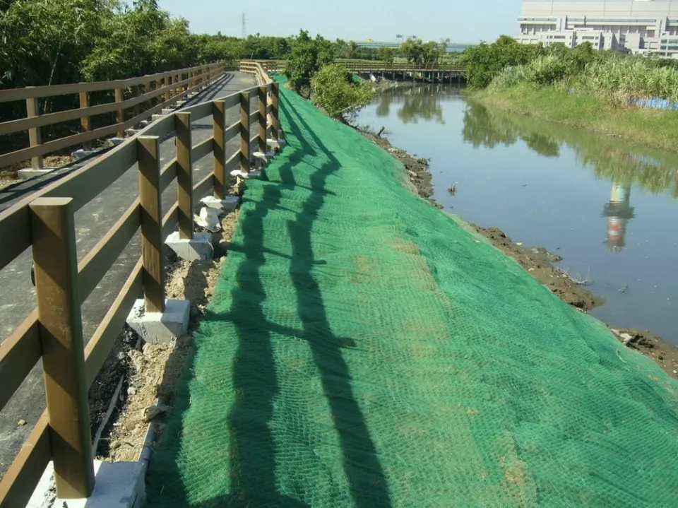 水岸步道旁,綠色網材覆蓋在堤坡上,另一側是水道