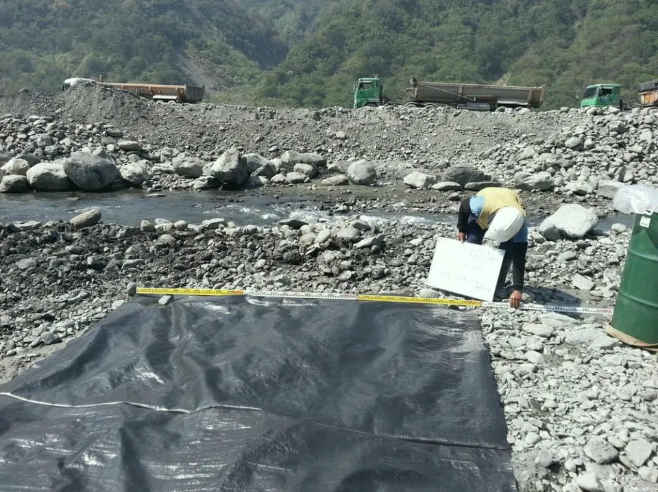 河床卵石間鋪設的深色織布,一位人員在旁量測記錄