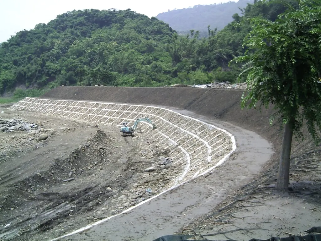 蜂巢格框護坡施工現場：坡面鋪設白色格框，一部怪手在坡上作業