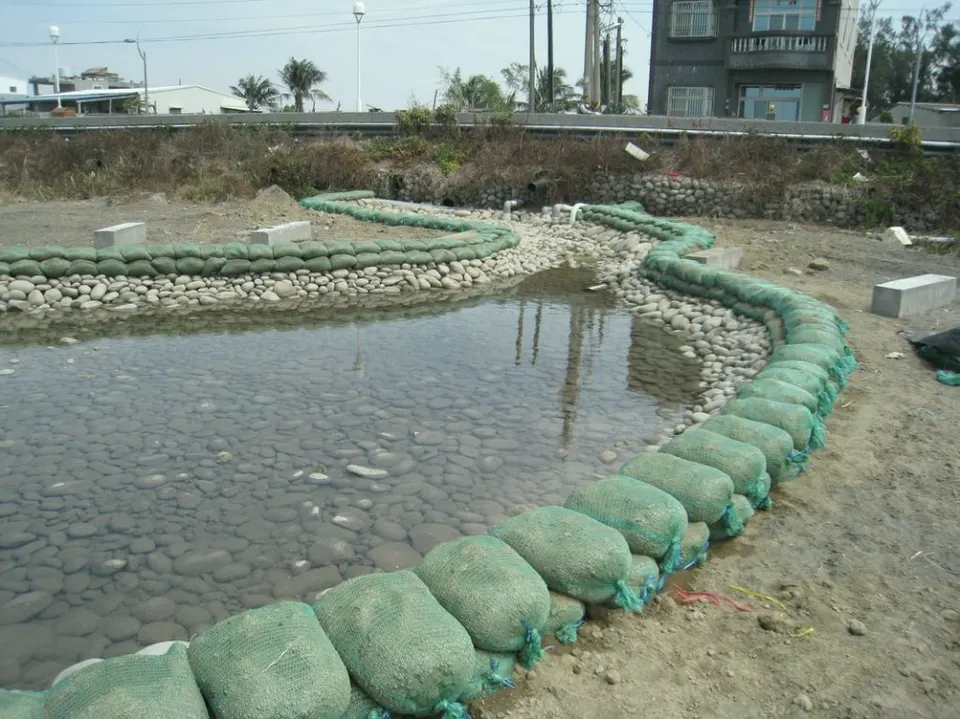 水池周圍以綠色袋體堆成弧形圍堰,池中有卵石